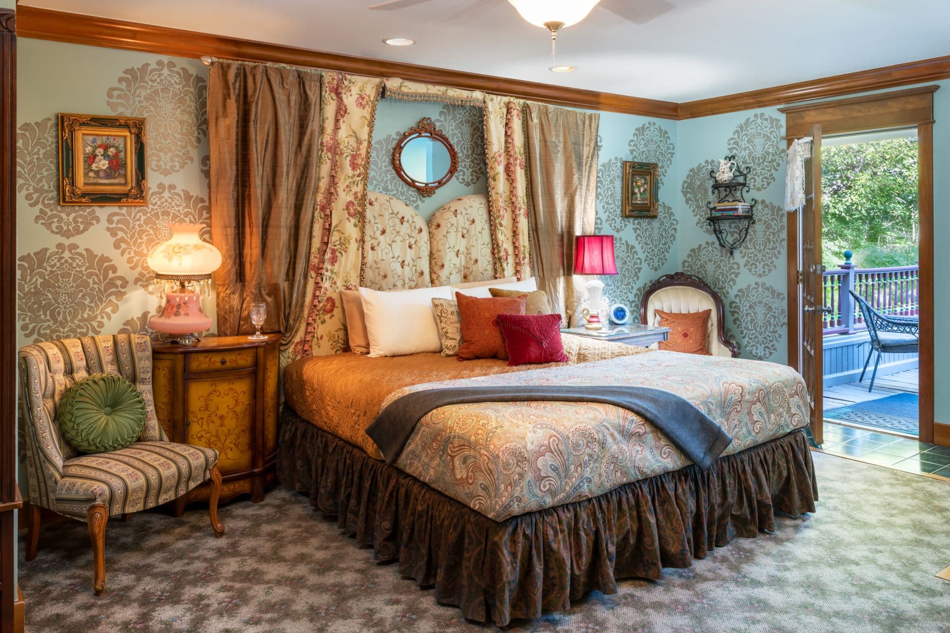 Luxurious bedroom with a king bed with designer linens flanked by comfortable armchairs and nightstands with table lamps. There is a doorway providing access to this room's private balcony.