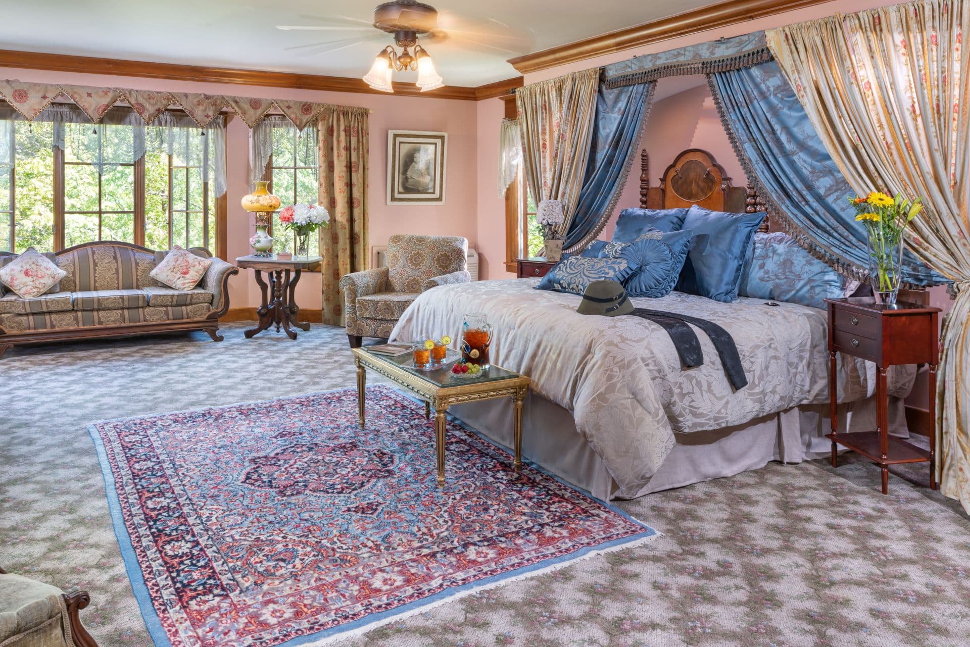 Luxurious bedroom with sumptuously draped king bed and upholstered sofa and armchair in front of a bank of windows with East Mountain views.