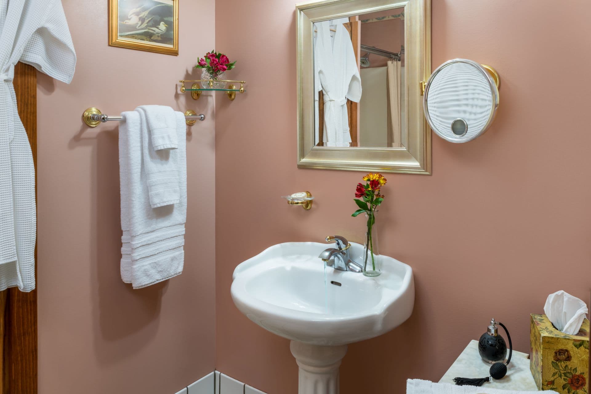 Bathroom with white pedestal sink, framed mirror, and plush white robe and towels hanging nearby.