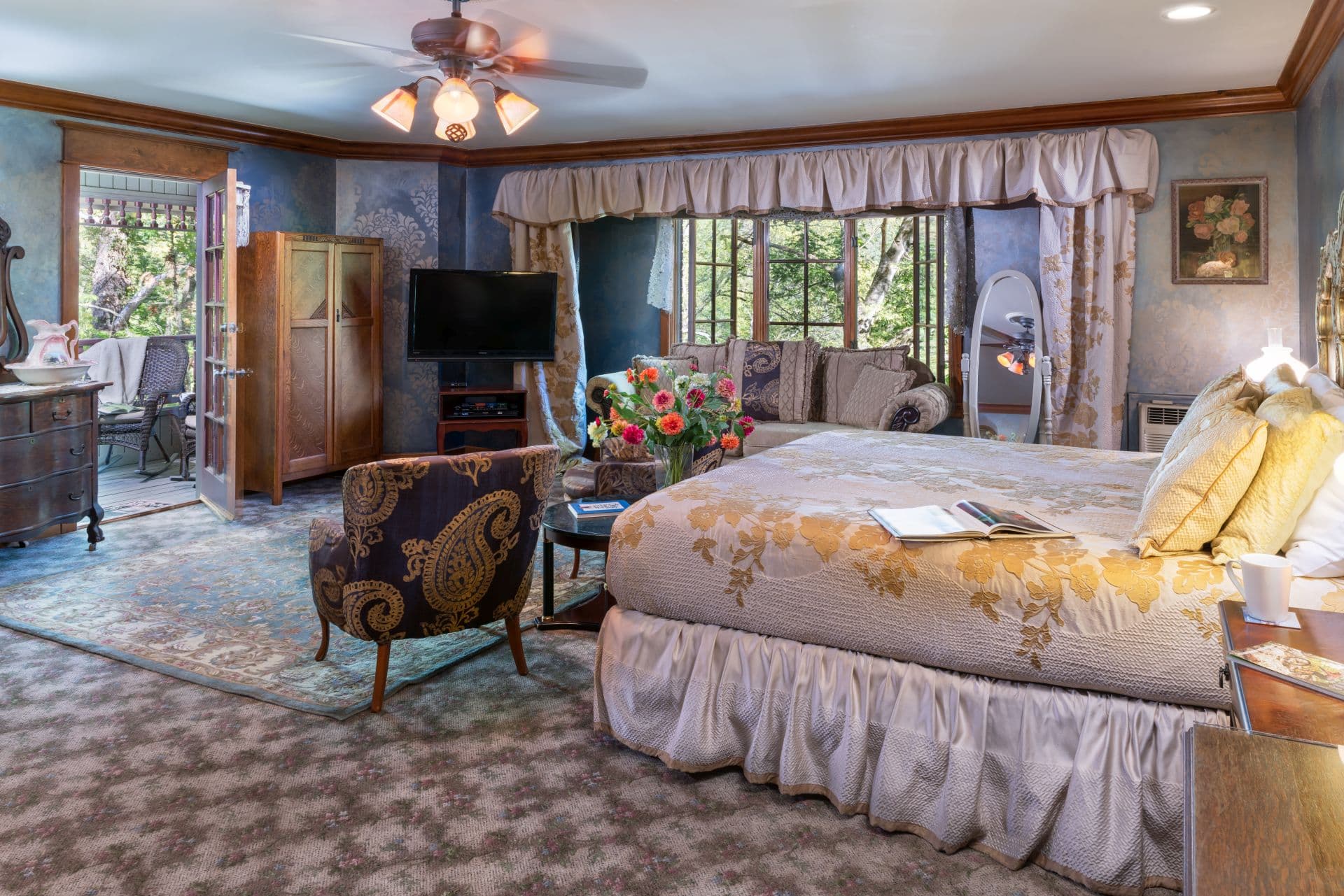 Luxurious Victorian bedroom with king bed, flat-screen TV, comfortable sitting area, and ceiling fan.
