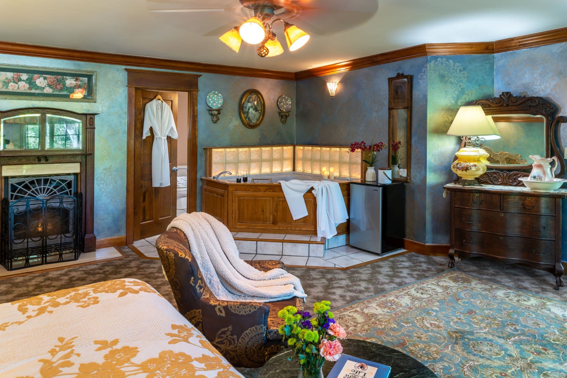 Spacious bedroom with fireplace, corner Jacuzzi tub, and ornate antique dresser with mirror.