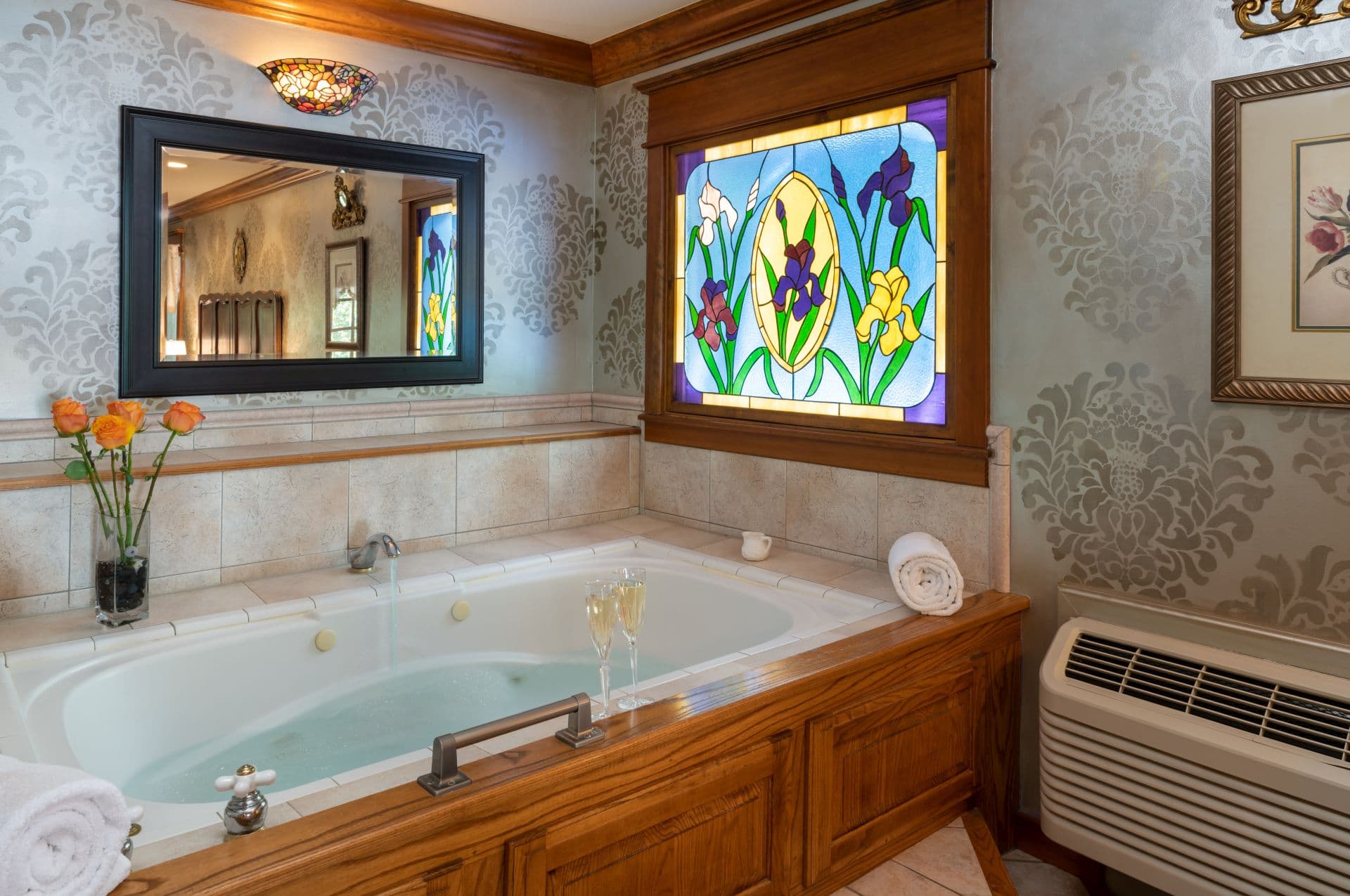 Jacuzzi soaking tub with lit with natural light shining through stained glass window featuring yellow and purple irises.