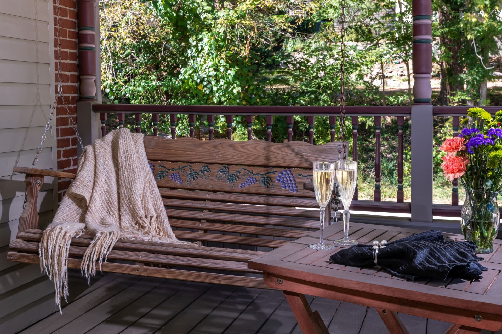 Private balcony with swing next to a table set with champagne flutes and a vase of fresh flowers.