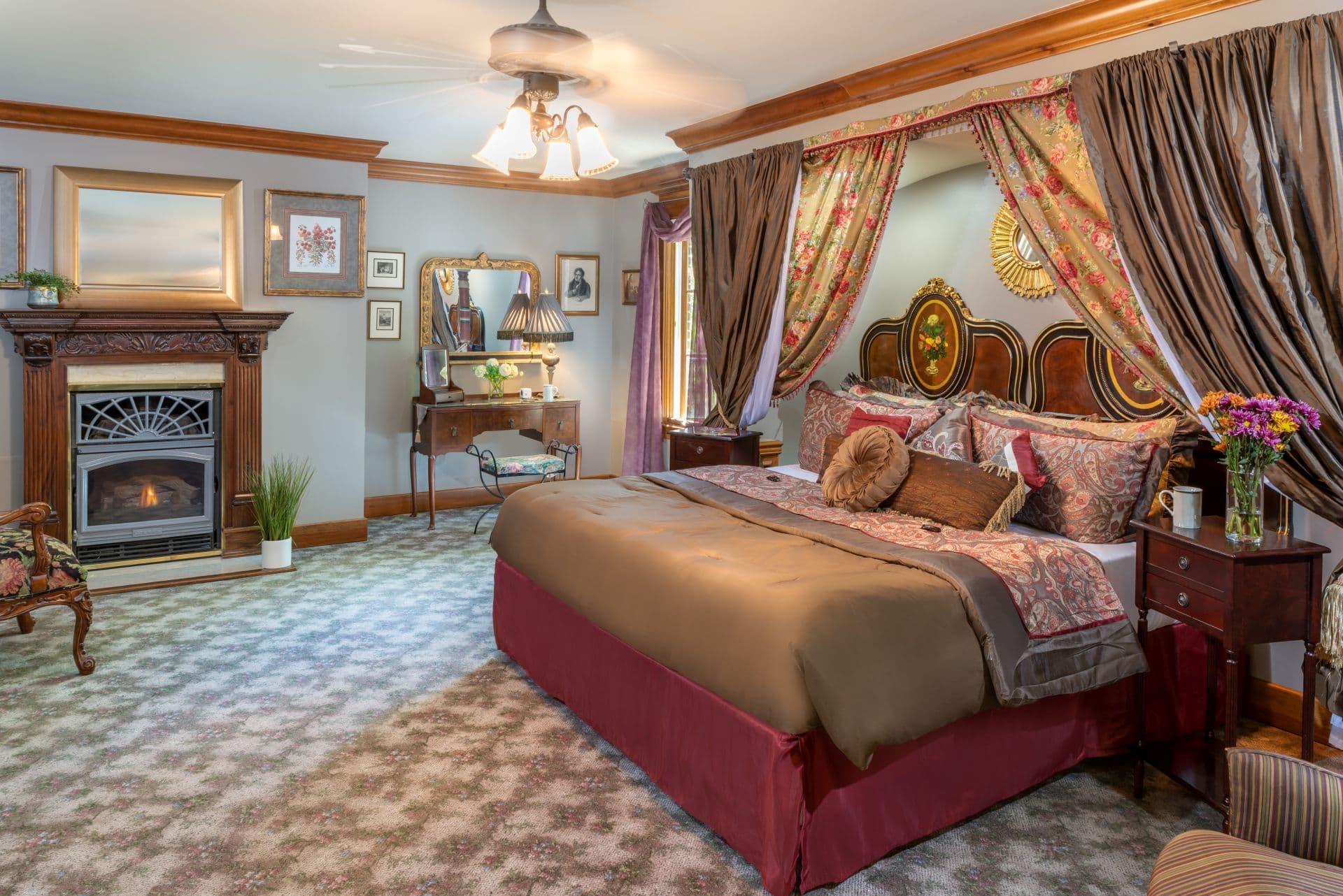 Luxurious bedroom with elegant king-size bed draped with designer linens. There is also a fireplace with a hand-carved mantle.