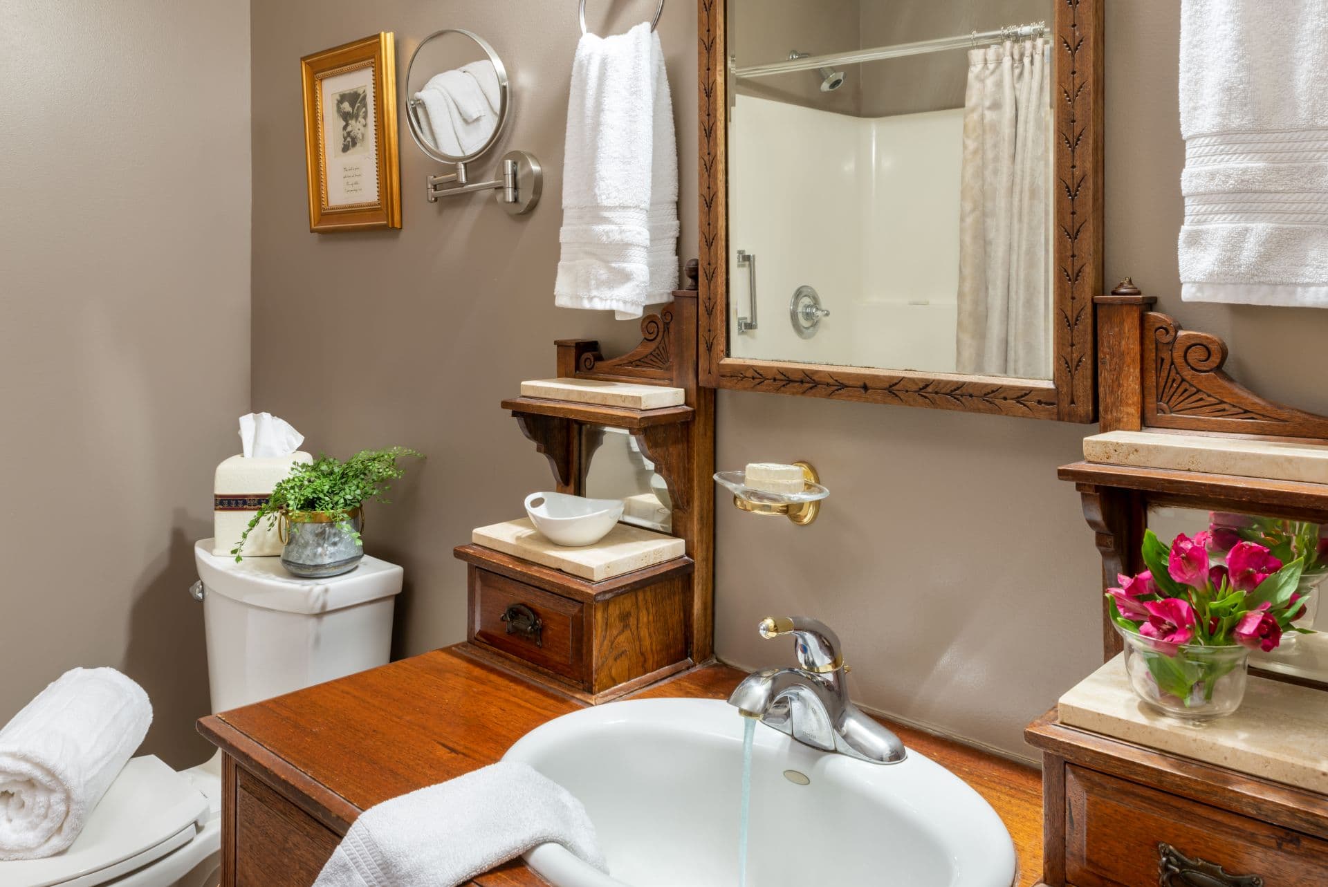 Bathroom with antique vanity with mirror, toilet, and plush white towels hanging nearby.