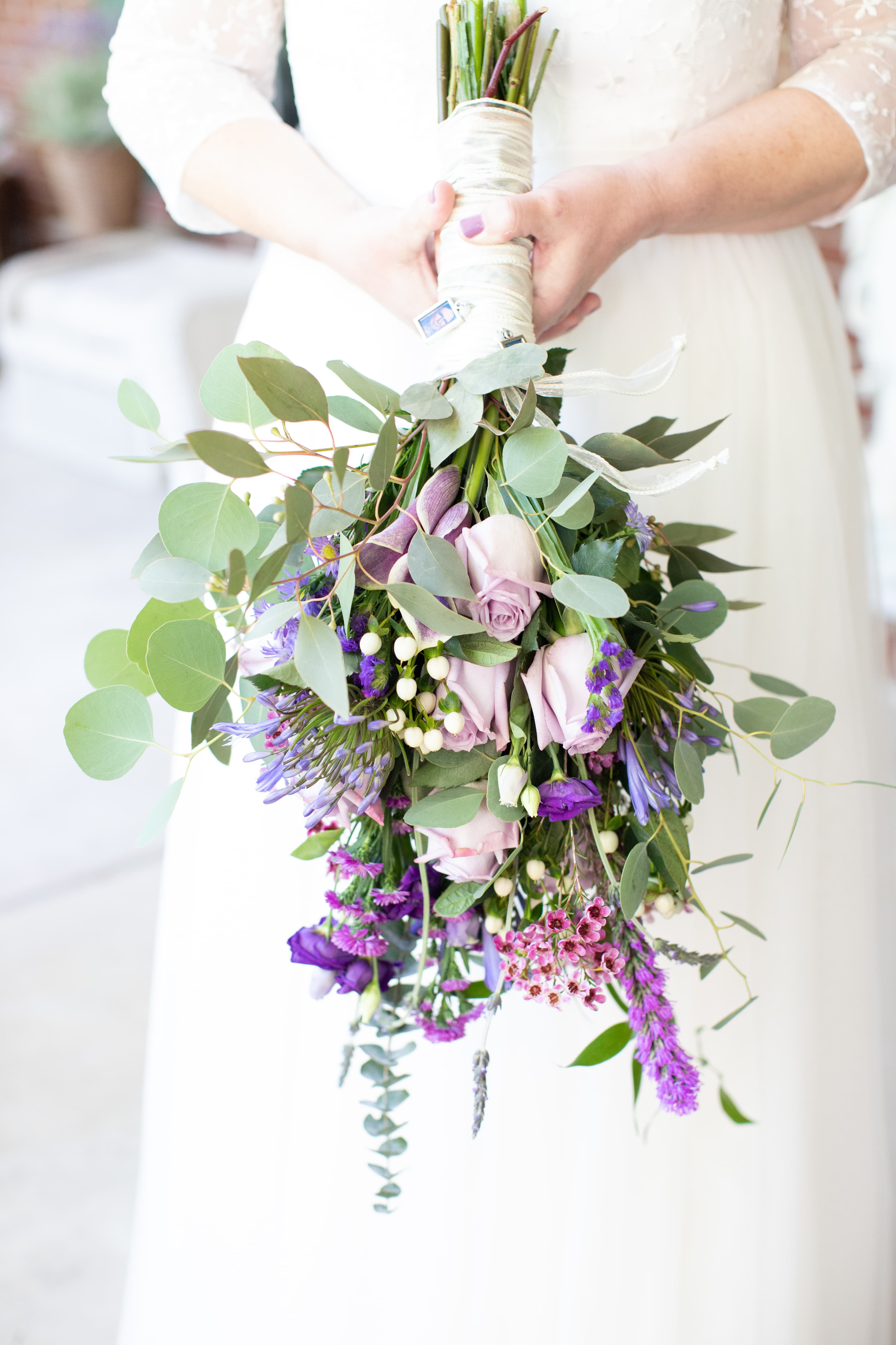 A close-up of a bridal bouquet featuring purple and pink flowers, surrounded by greenery.