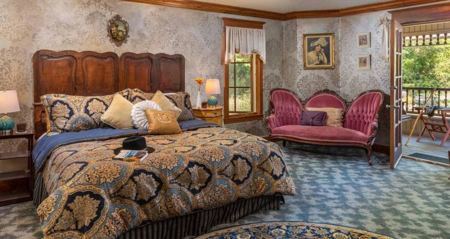 A cozy, elegantly decorated bedroom featuring a vintage bed, decorative pillows, and a pink loveseat by the window.