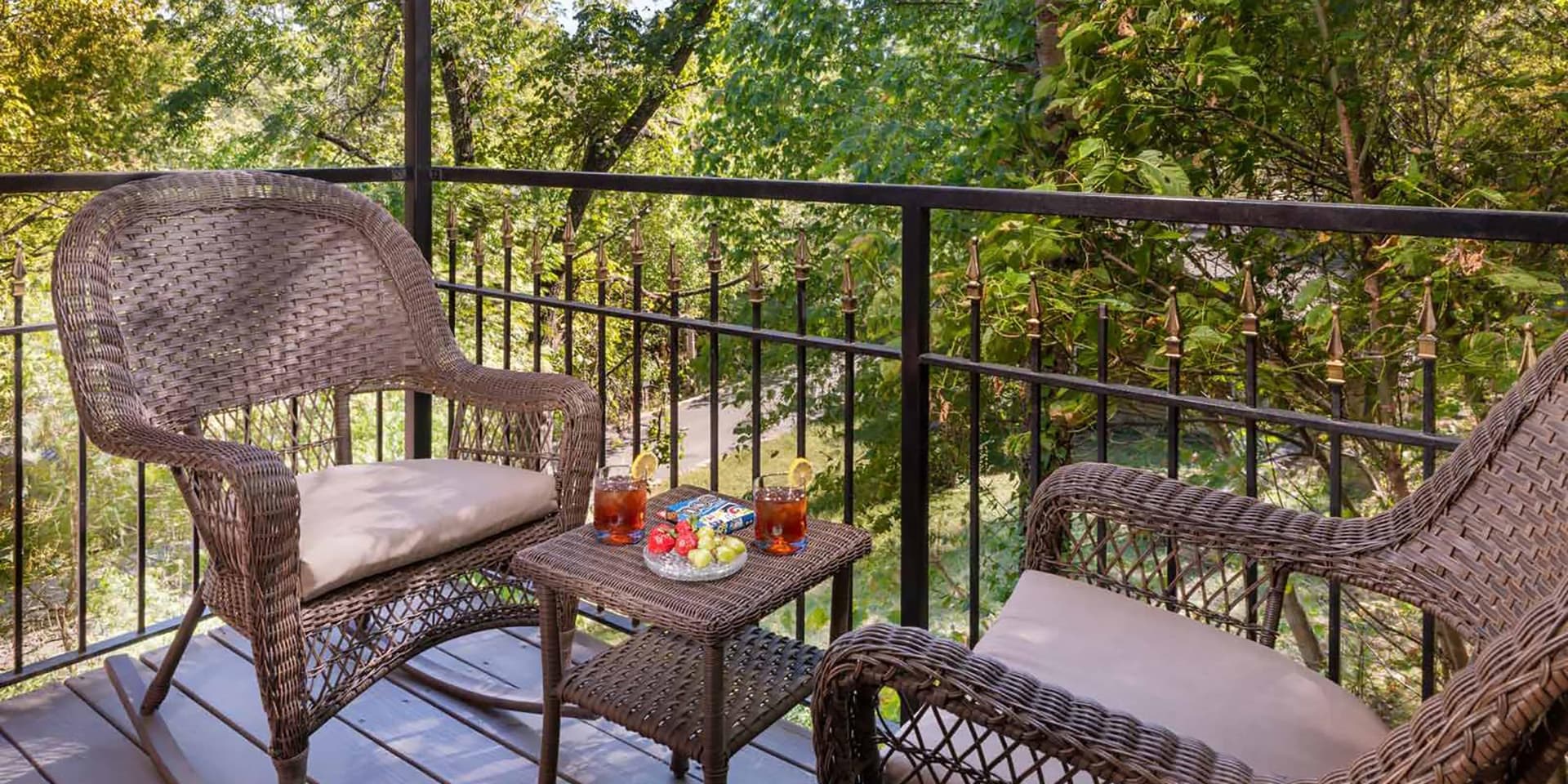 A cozy balcony with wicker chairs, a small table with drinks and snacks, surrounded by greenery.