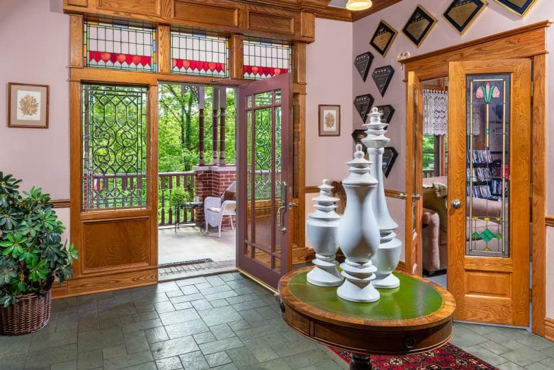 A bright foyer featuring stained glass windows, a round table with white vases, and an open door leading to a balcony.