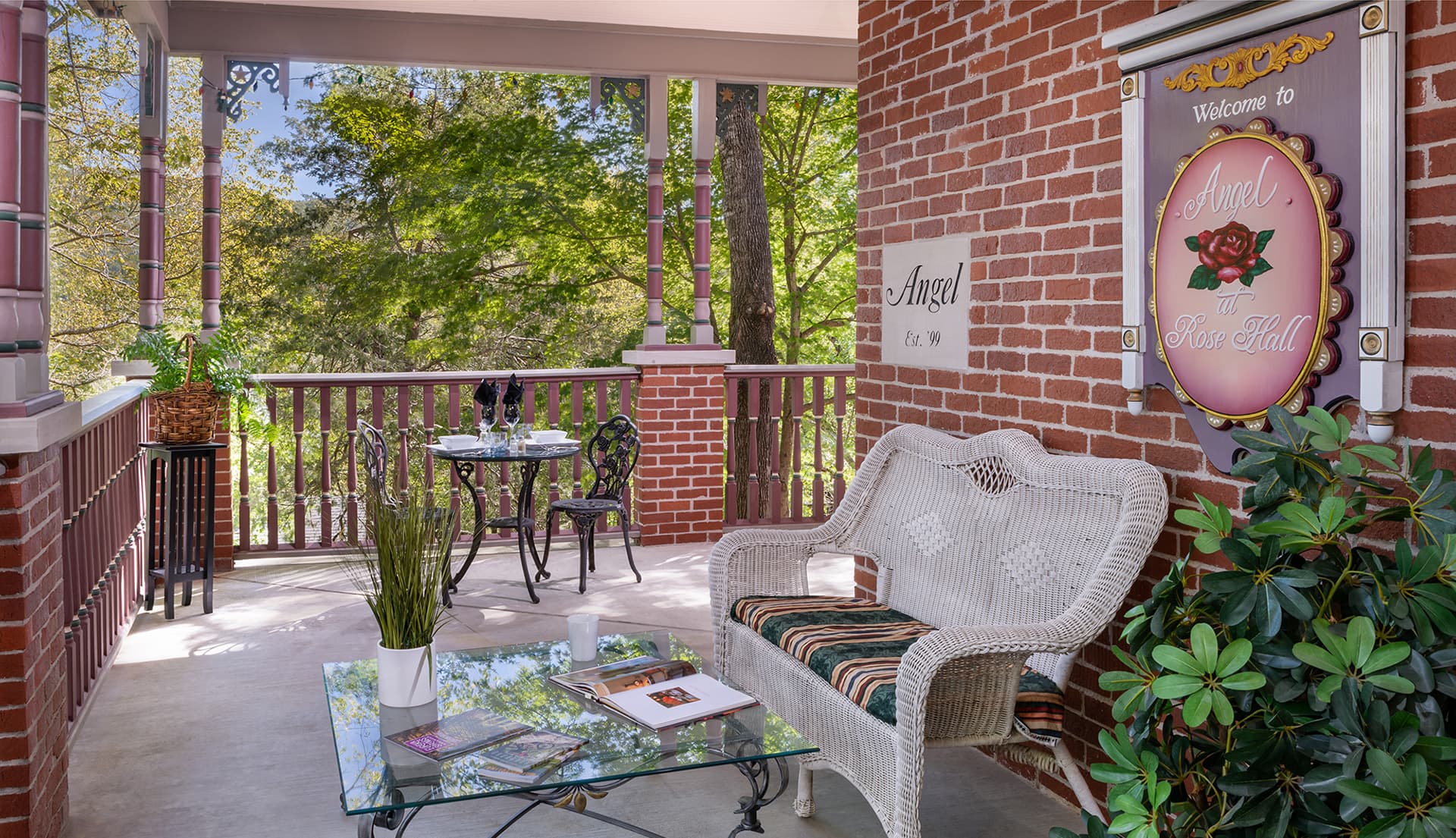 A cozy porch featuring a wicker seat, glass table with magazines, and a decorative sign welcoming visitors.