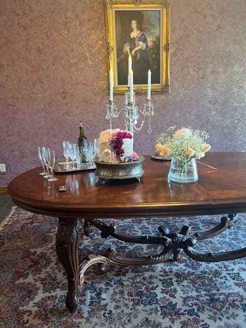 A beautifully set dining table with a floral centerpiece, glassware, candles, and a framed portrait in the background.