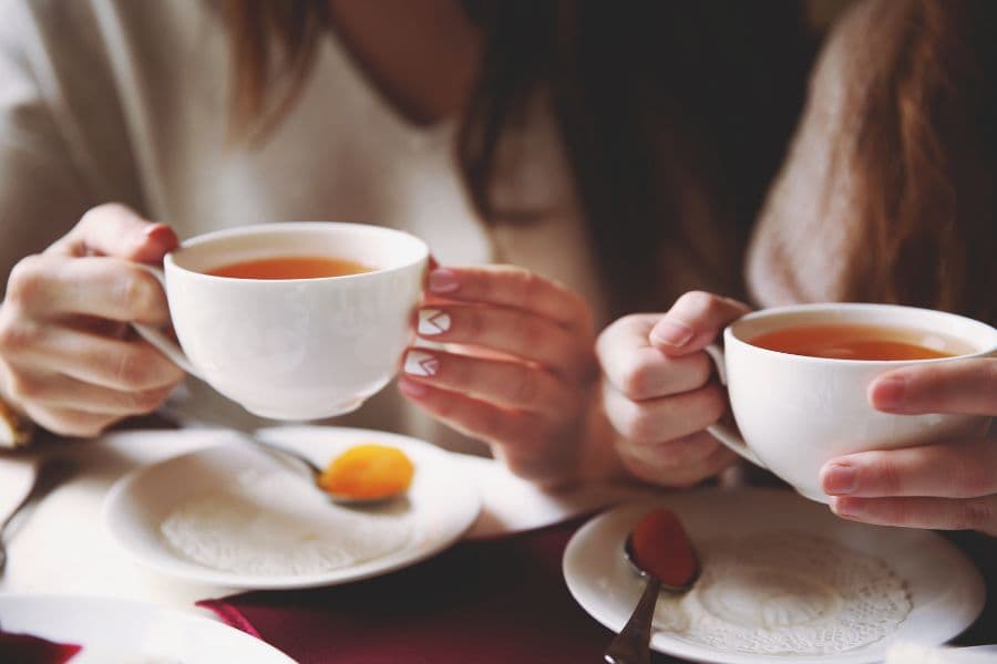 Two people holding tea cups at a table with a small plate and spoon.