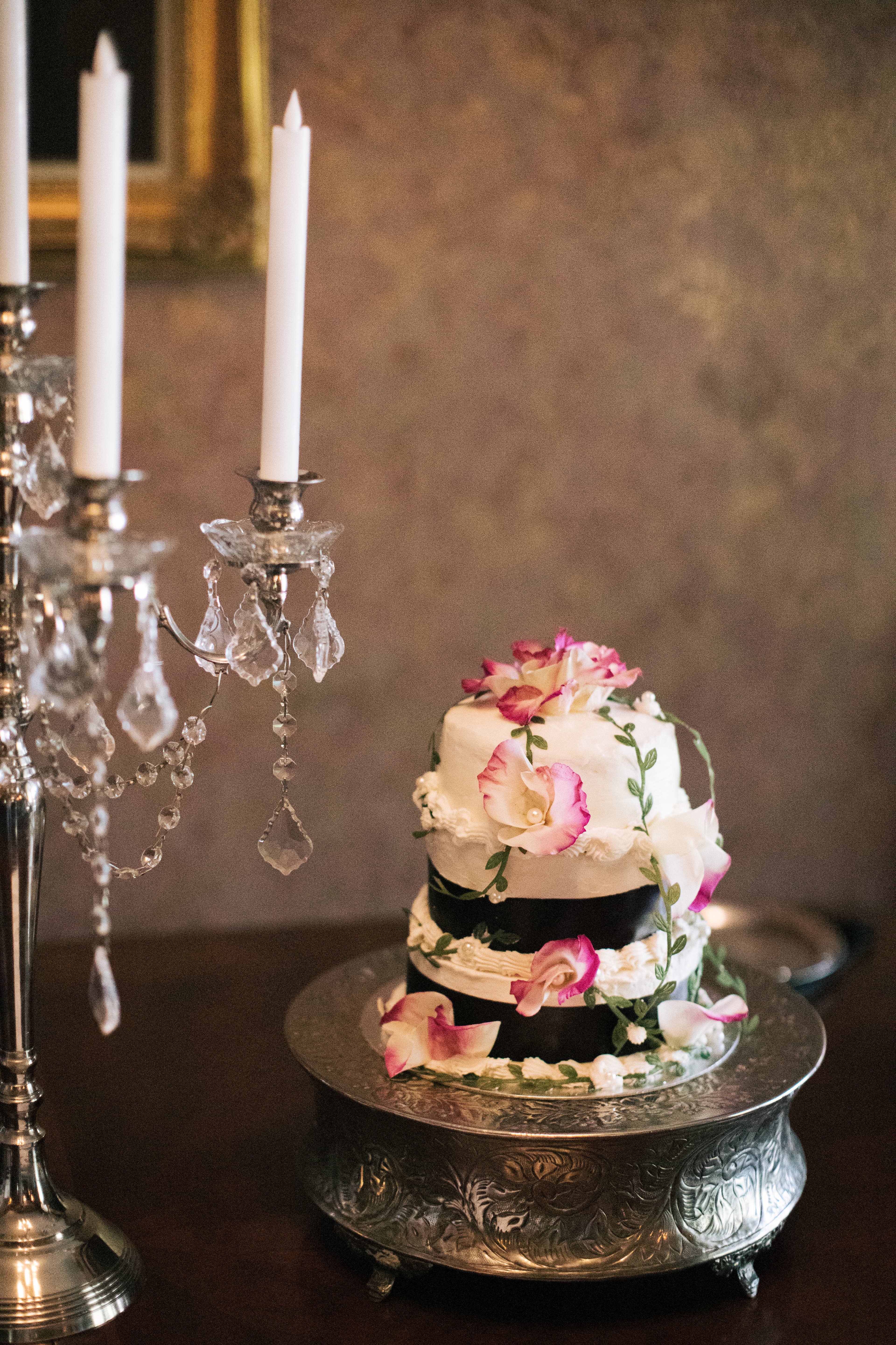 A three-tier wedding cake adorned with pink flowers sits beside a silver candelabra.